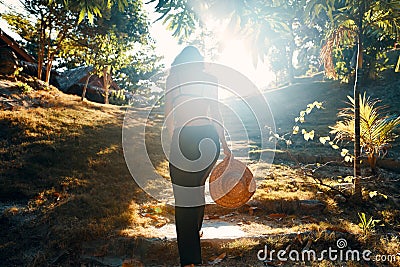 Back view of young woman in straw hat rwalking up stairs in green tropical park in sun light Stock Photo