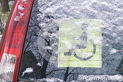 Back window of a car with the Disabled driving yellow sign. Covered with wet snow and water drops. The information sign says the c Stock Photo