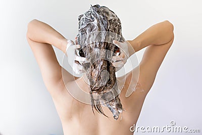 The back of a woman washing her hair full of suds in front of a white background. Stock Photo