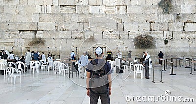 Back of a young tourist in casual clothes and kippah on the head looking at the wailing wall and religious praying near the sacred Editorial Stock Photo