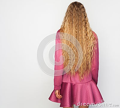 Back of the young woman with long blond curly hair with healthy shine, wearing a purpl dress over a studio background. Stock Photo