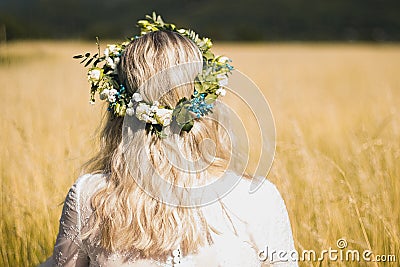 Back of the young woman in a white dress in boho style with a floral wreath in the summer in the field Stock Photo
