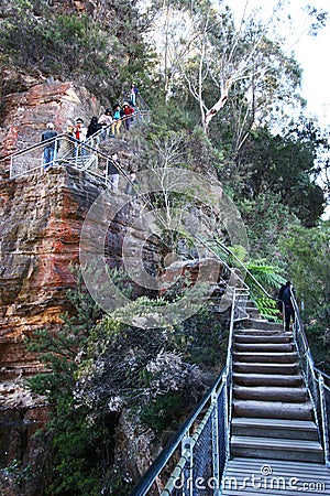 Tourists hiking at steep zigzag trail of Grand Stairway along red rock shear cliff with vegetation in Blue Mountains National Park Editorial Stock Photo