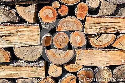 Background of ends of logs and dry firewoods. Close-up of outdoor stack of wood on a sunny day. Folded and packaged firewood. Stock Photo