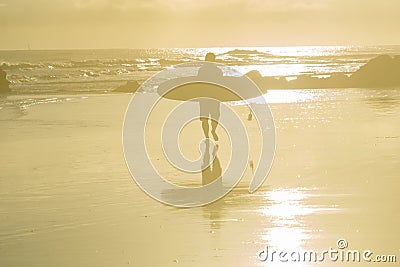 Background faded image of surfer walking into sunrise and water carrying surfboard Stock Photo