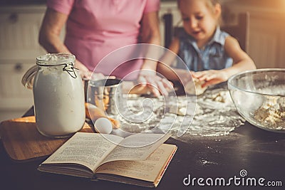 Background image cookbook, table, rolling pin, focus on the foreground. Girl and her grandmother cooking on kitchen. Stock Photo