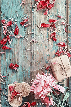 Background with pink peony, peonies petals, gift box and a wooden heart on old green boards. Stock Photo