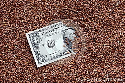 The background texture of a large pile of buckwheat, in the middle of which you see a bill of one US dollar. The concept of highe Stock Photo