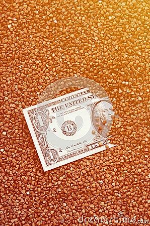 The background texture of a large pile of buckwheat, in the middle of which you see a bill of one US dollar. The concept of highe Stock Photo