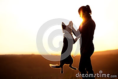 Backlight Silhouette of a woman with her jumping dog, playing on Stock Photo