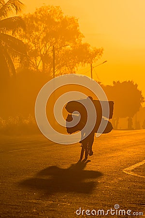 A backlit Mozambican cyclist with dramatic shadow, carrying a heavy load of coal Stock Photo