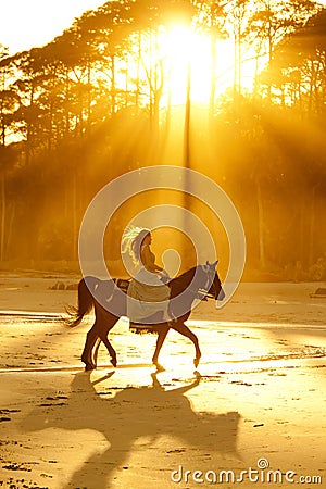 Backlit woman riding horse on beach Stock Photo