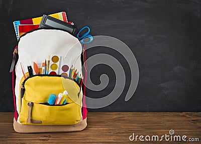 Backpack full of school supplies over black school board background Stock Photo