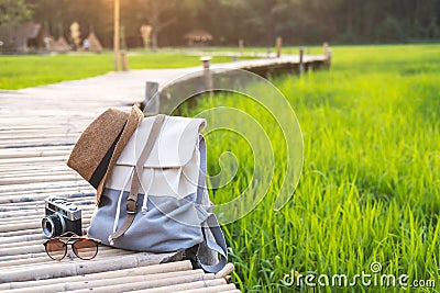 Backpack with hat and camera on bamboo path at green paddy field Stock Photo