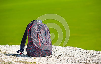 Backpack on white rock on green fresh drass background. Sunny gay travelling concept. Place for text. Stock Photo