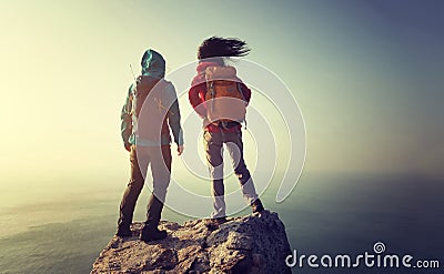 Backpackers stand on sunrise seaside mountain top rock edge Stock Photo