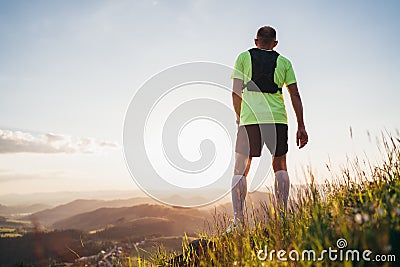Backview of Active mountain trail runner dressed bright t-shirt with backpack enjoying the sunset while he sky running by Stock Photo