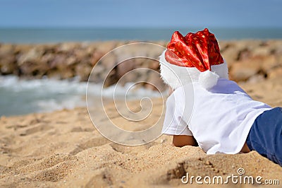 Backview of child in Santa hat lying on sand shore Stock Photo