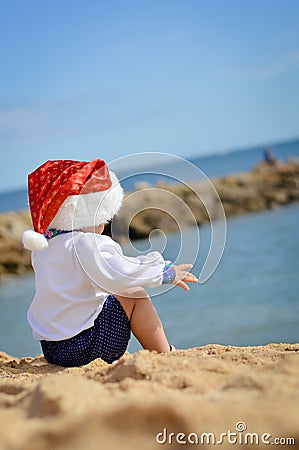 Backview of child in Santa hat sitting on seashore Stock Photo