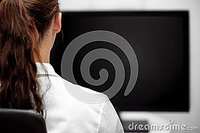 Backview, young lab assistent or female doctor looking at a black desk or monitor Stock Photo