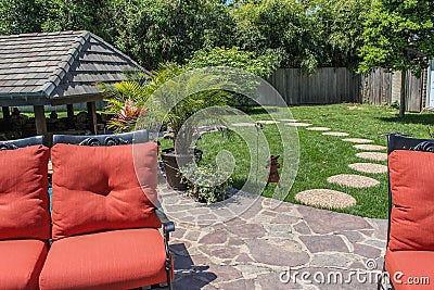 Backyard garden with patio and stepping stones to covered outdoor living area - orange cushioned lawn furniture in foreground with Stock Photo