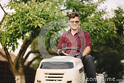 Backyard lawncare man portrait - Smiling worker using ride on grass mower Stock Photo