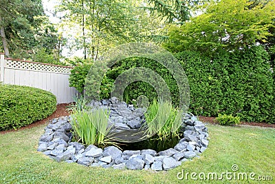 Backyard pond with grey rocks and green fenced yard. Stock Photo