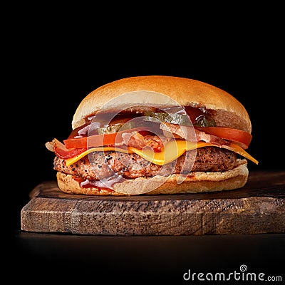 Bacon Burger, tomato on wooden cutting board, isolated on dark background Stock Photo