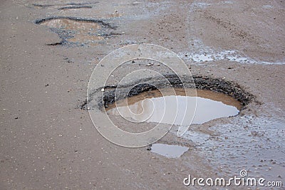 The bad asphalted road with a big pothole filled with water. Dangerous destroyed roadbed. Stock Photo