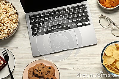 Bad eating habits at workplace. Laptop, glasses and different snacks on white wooden table, flat lay Stock Photo