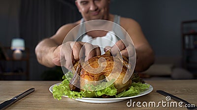 Bad-mannered overweight man tearing piece of chicken with hands, overeating Stock Photo