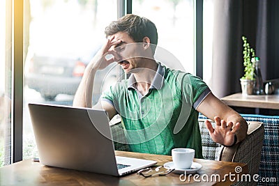 Bad smell. Young dissatisfied businessman in green t-shirt sitting and working on laptop, pinching his nose with negative emotion Stock Photo