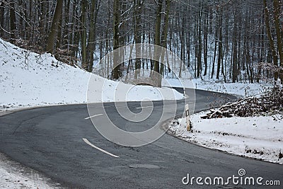 badly damage road with a downhill s-curve in winter forest Stock Photo