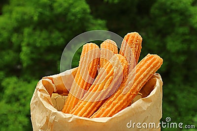 Bag of Delectable Fresh Fried Churros with Blurry Green Foliage in Background Stock Photo