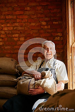 We bag our own beans. Cropped portrait of a senior man holding a sack of coffee beans while sitting in a roastery. Stock Photo