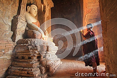 BAGAN, MYANMAR - May 2016: Monk burning candles in front of Buddha statue inside pagoda on May, 2016 in Bagan. Editorial Stock Photo