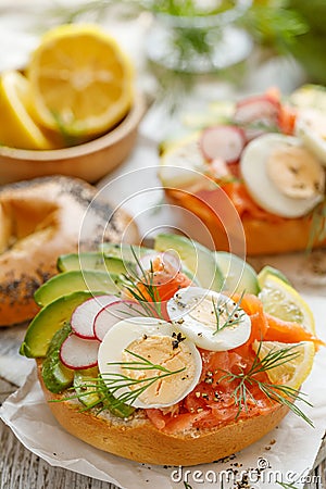 Bagel sandwich with smoked salmon, avocado, boiled eggs, radish, lemon and fresh dill on a wooden table Stock Photo