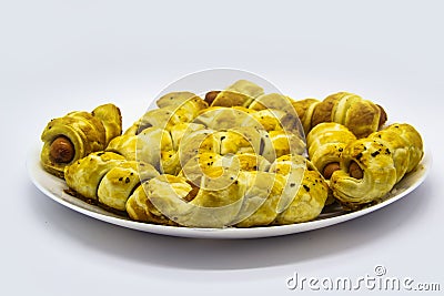 Baked ausages in the dough on a white plate against white background. Sausage Puff Pastry Buns.sausages wrapped in puff pastry and Stock Photo