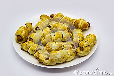 Baked ausages in the dough on a white plate against white background. Sausage Puff Pastry Buns.sausages wrapped in puff pastry and Stock Photo