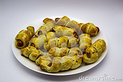 Baked ausages in the dough on a white plate against white background. Sausage Puff Pastry Buns.sausages wrapped in puff pastry and Stock Photo