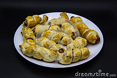 Baked ausages in the dough on a white plate against black background. Sausage Puff Pastry Buns.sausages wrapped in puff pastry and Stock Photo