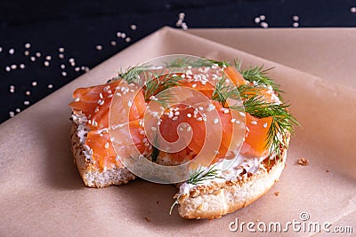 Baked bun, oiled with fresh cream, garnished with smoked fish trout and sprinkled with fresh dill and sesame seeds on parchment Stock Photo