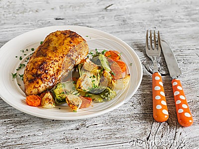 Baked chicken breast with brussels sprouts, onions and carrots on a white plate on wooden surface. Stock Photo