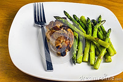 Baked chicken thigh served with sauteed asparagus Stock Photo