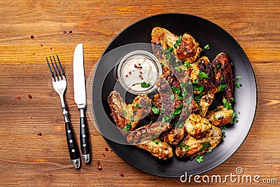 Baked chicken wings in Mexican with curry seasoning and parsley on a black plate, on a wooden background. side view, copy space Stock Photo