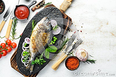 Baked Dorado fish with vegetables on a black stone plate. Top view. Stock Photo