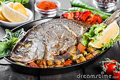 Baked dorado fish with vegetables and lemon on pan on wooden background close up Stock Photo