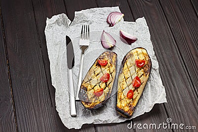 Baked eggplant with onions and tomatoes, knife and fork on paper Stock Photo