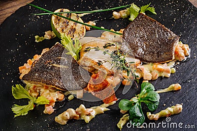Baked plaice fillet with vegetables and sauce close-up on a bla Stock Photo