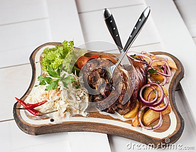 Baked pork knuckle with sauerkraut, potatoes, onions and greens on a wooden cutting board Stock Photo